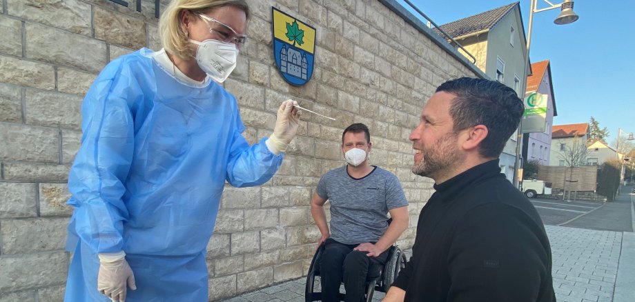 Das Bild zeigt Apothekerin Marta Martin und Bürgermeister Martin Finzel bei einem ersten symbolischen Schnelltest vor dem Bürgerhaus Linde. Im Hintergrund Geschäftsleiter Michael Goebbel.